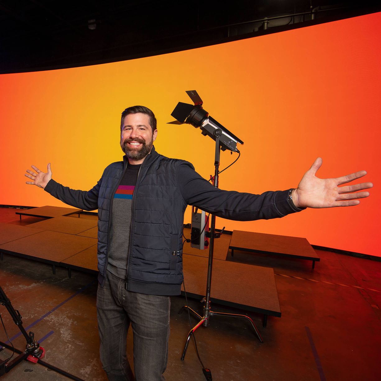 A man with his arms outstretched in front of a large orange screen.